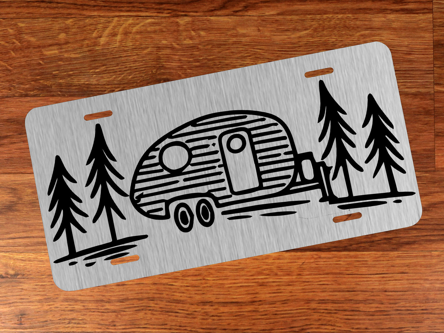 Metallic license plate with camper and tree design on a wooden surface