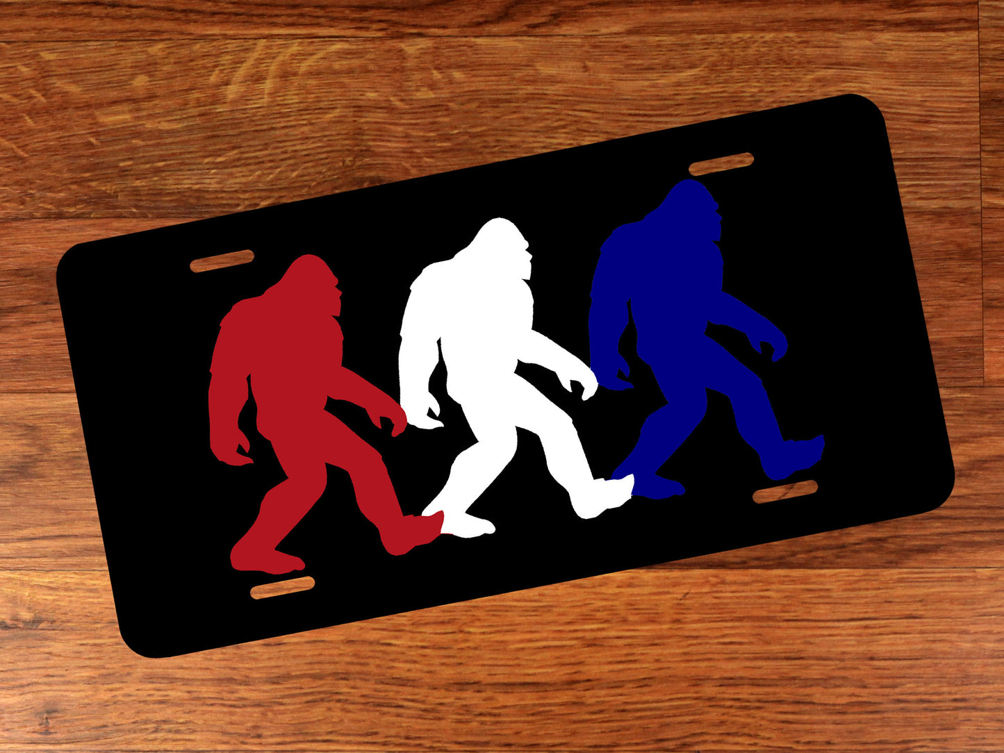 Black license plate with red, white, and blue Bigfoot silhouettes on a wooden surface