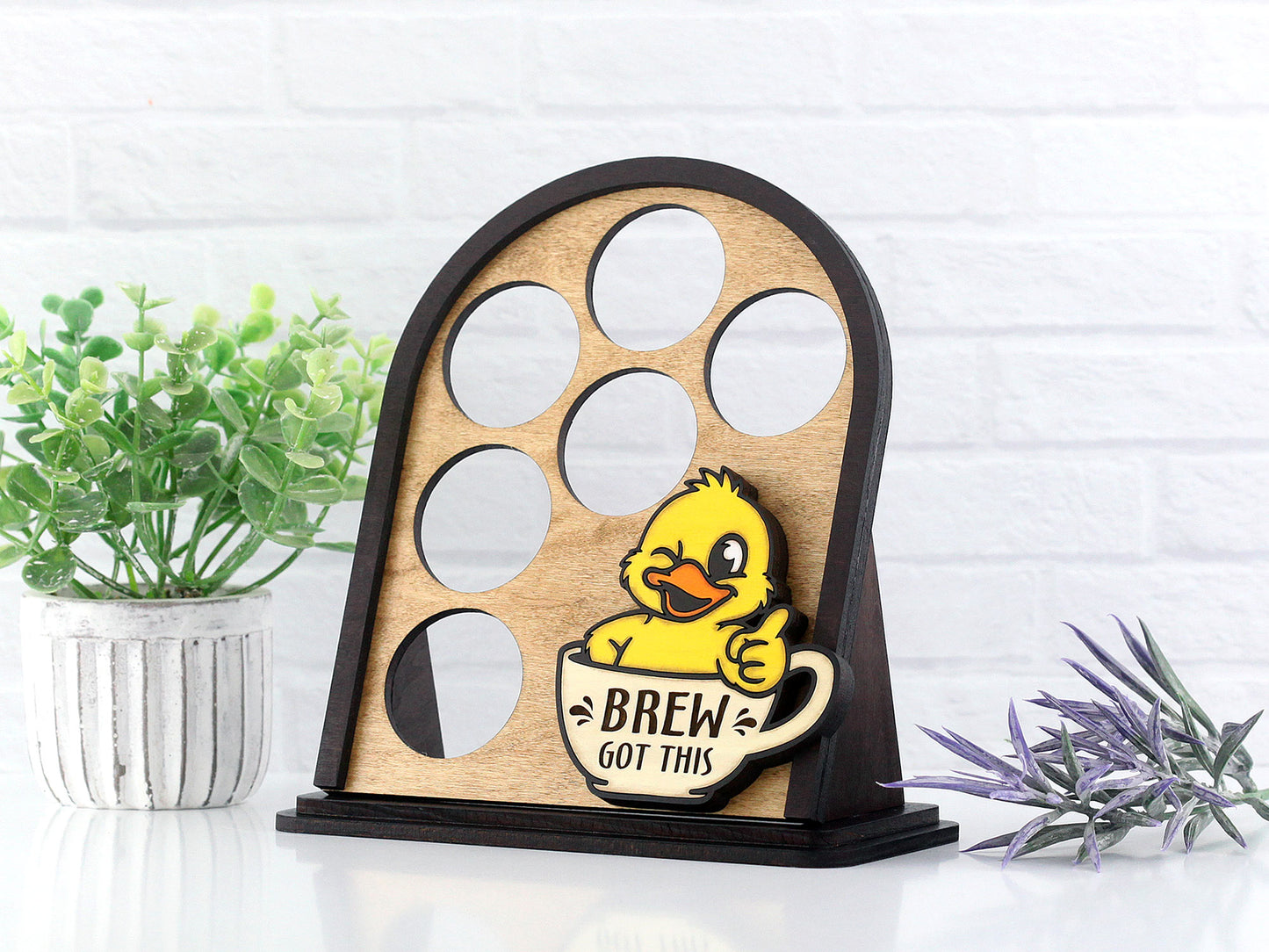 Wooden coffee pod organizer with a duck design and 'Brew Got This' text, placed on a white surface with plants.