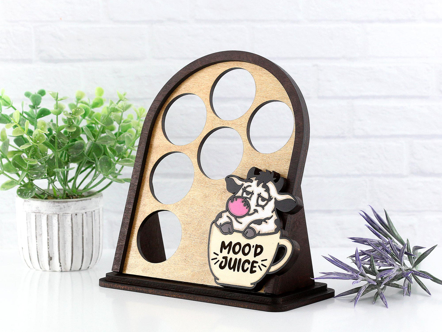 Wooden k cup holder with cow design and 'Mood Juice' text, placed on a white surface with plants.
