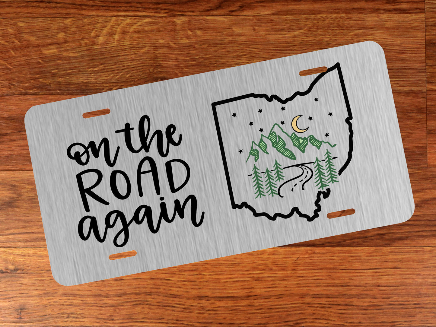 License plate with 'on the road again' text and Ohio outline design on a wooden surface