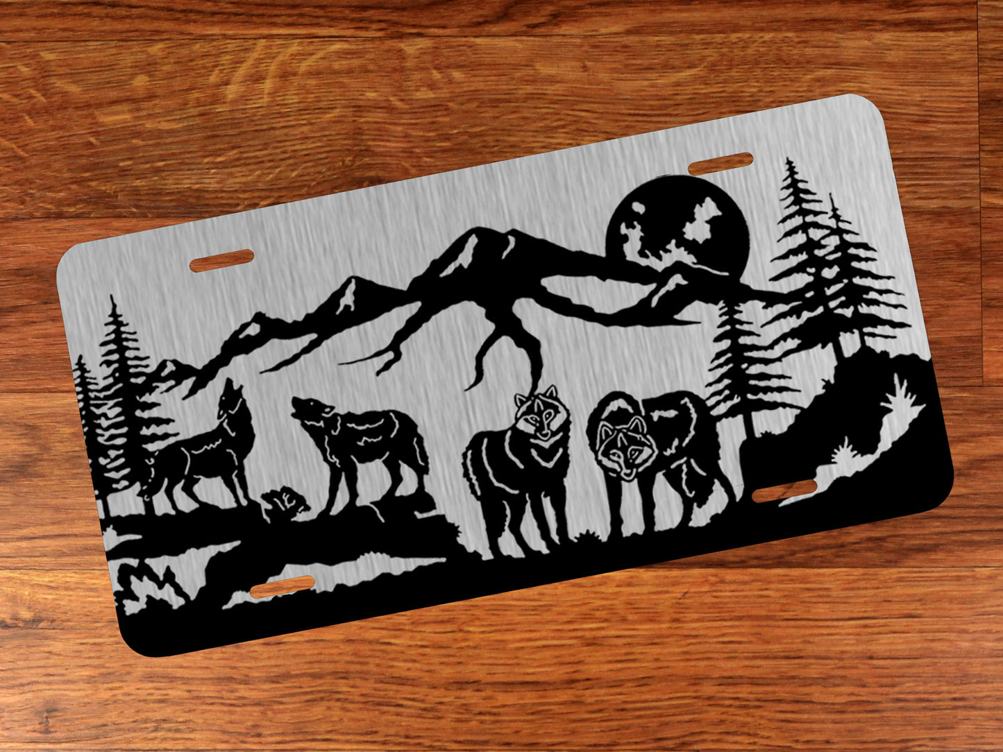 Decorative license plate with wolf and mountain design on silver against a wood background