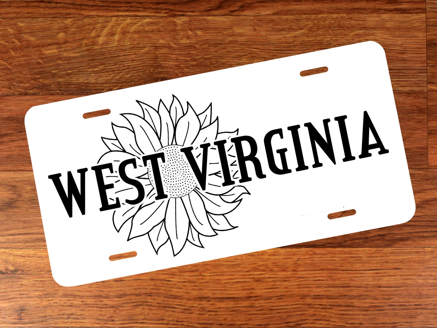 White license plate with black 'West Virginia' text and sunflower design on a wooden surface