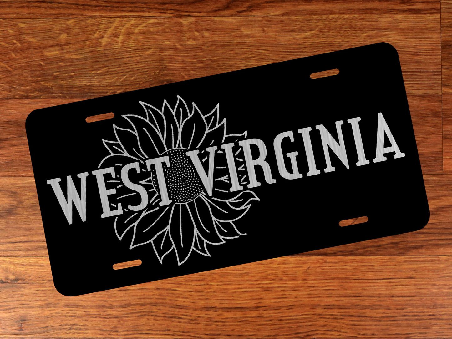 Black on silver license plate with sunflower design and 'West Virginia' text on a wooden surface