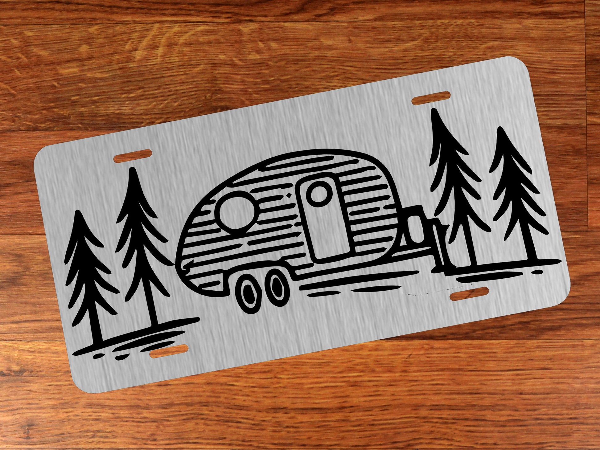 Metallic license plate with camper and tree design on a wooden surface