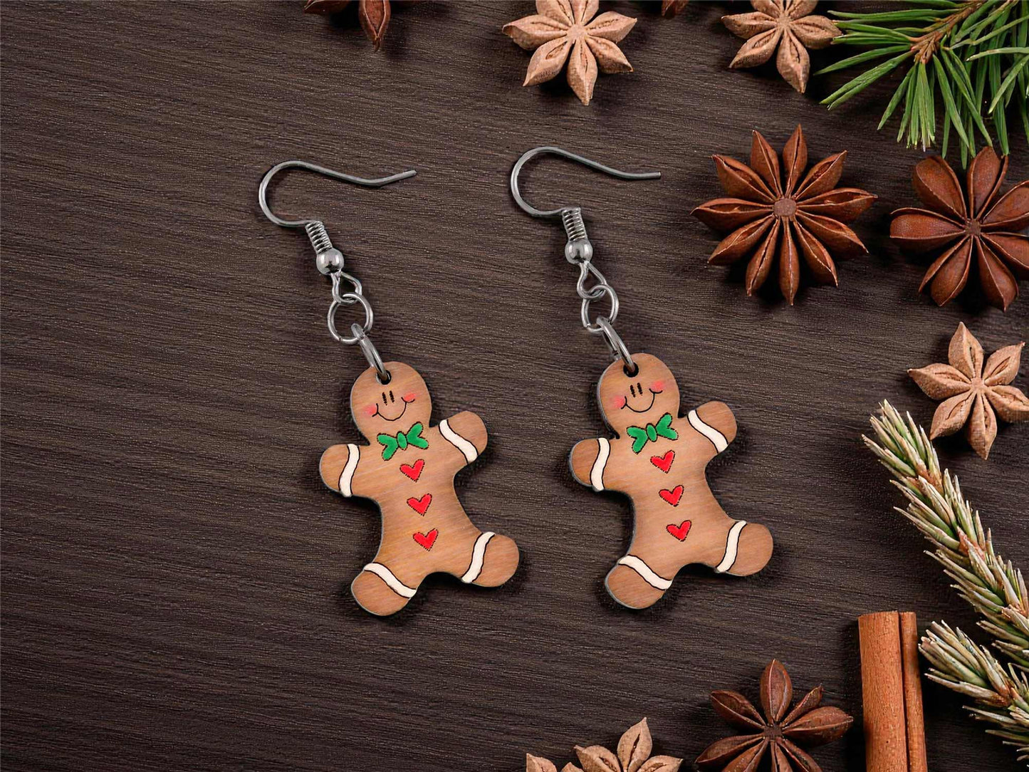 Gingerbread man earrings on a wooden surface with star anise and cinnamon sticks.