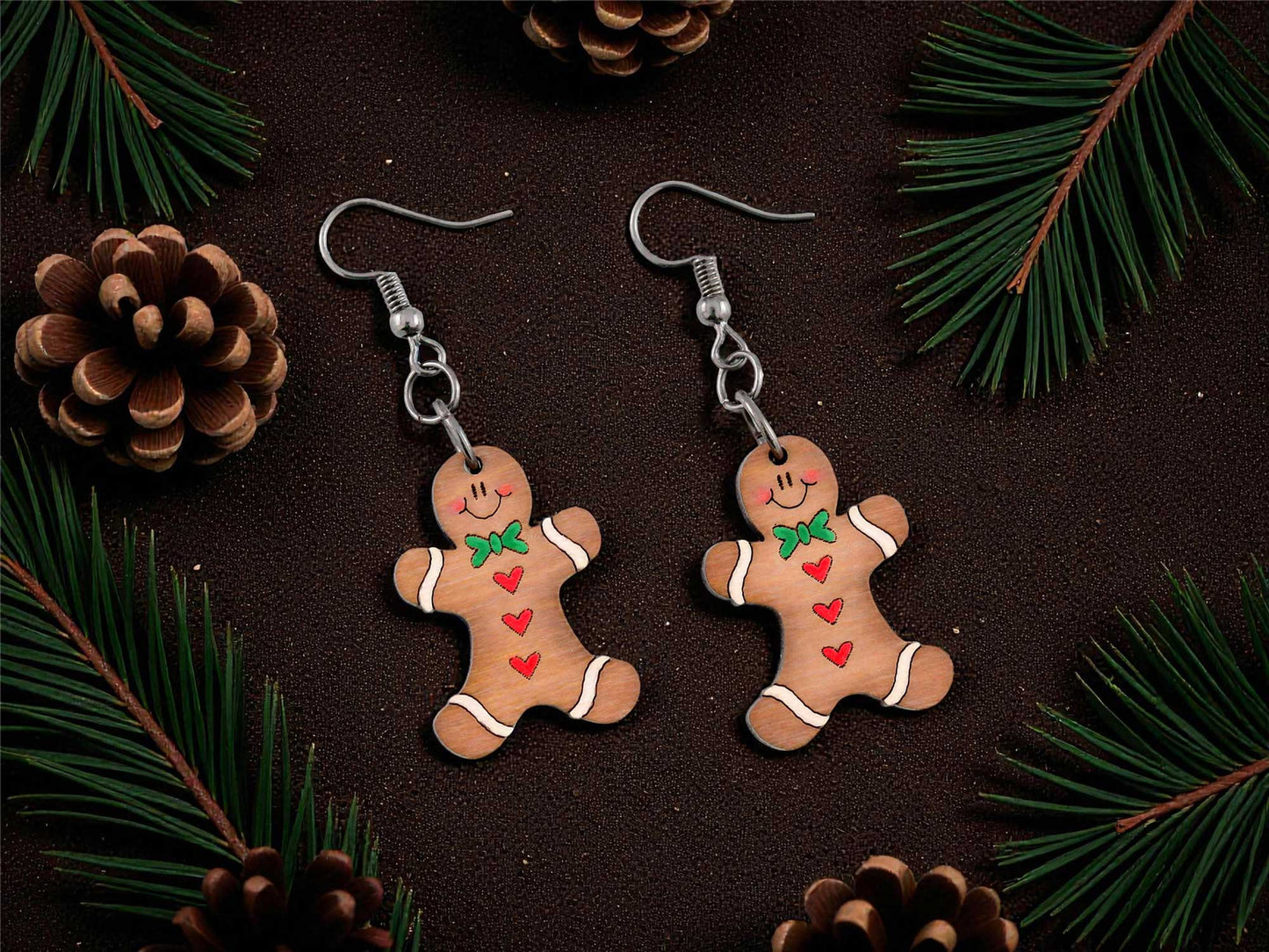 Gingerbread man earrings on a dark surface with pine branches and cones.