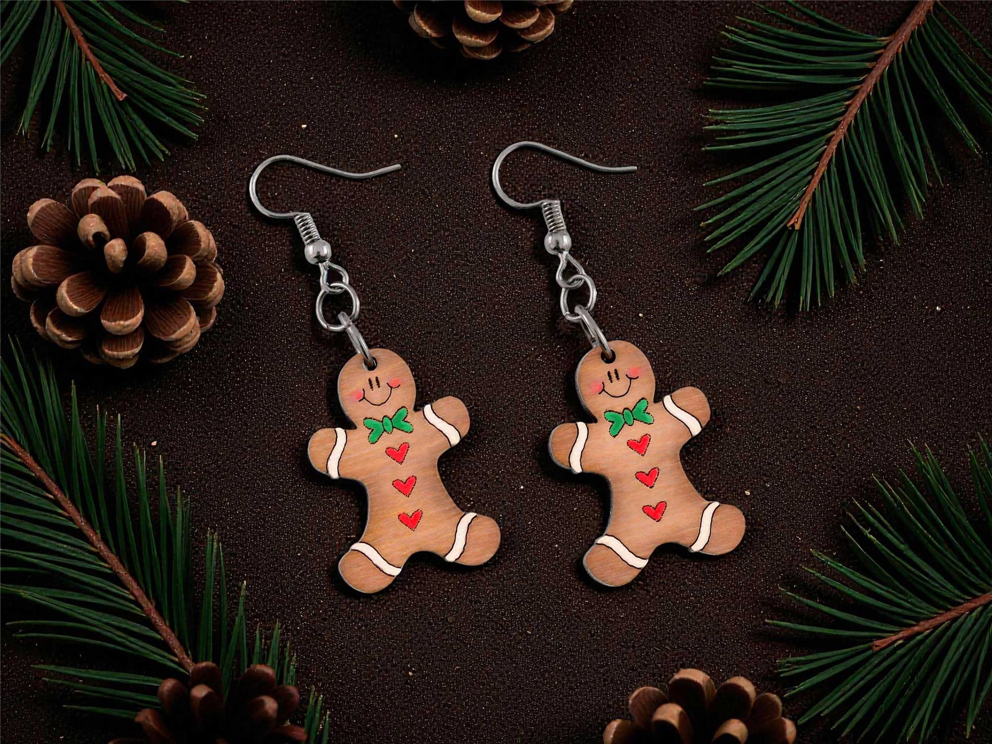 Gingerbread man earrings on a dark surface with pine branches and cones.