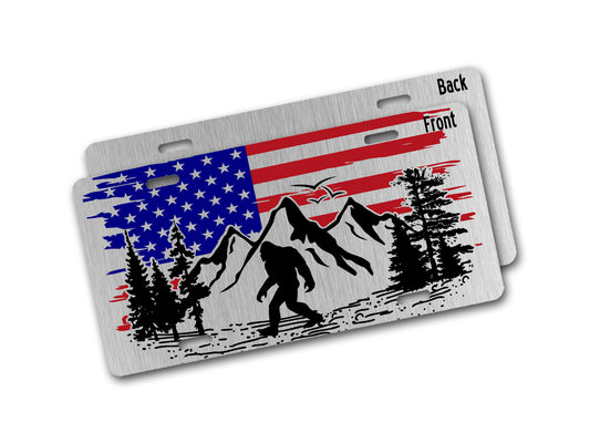Aluminum license plate with American flag, mountains, and a Sasquatch design on a white background.