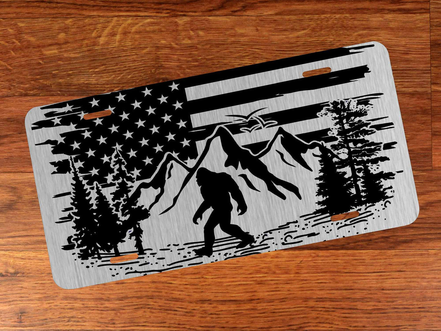 License plate with American flag, mountains, and a Sasquatch design on a wooden surface
