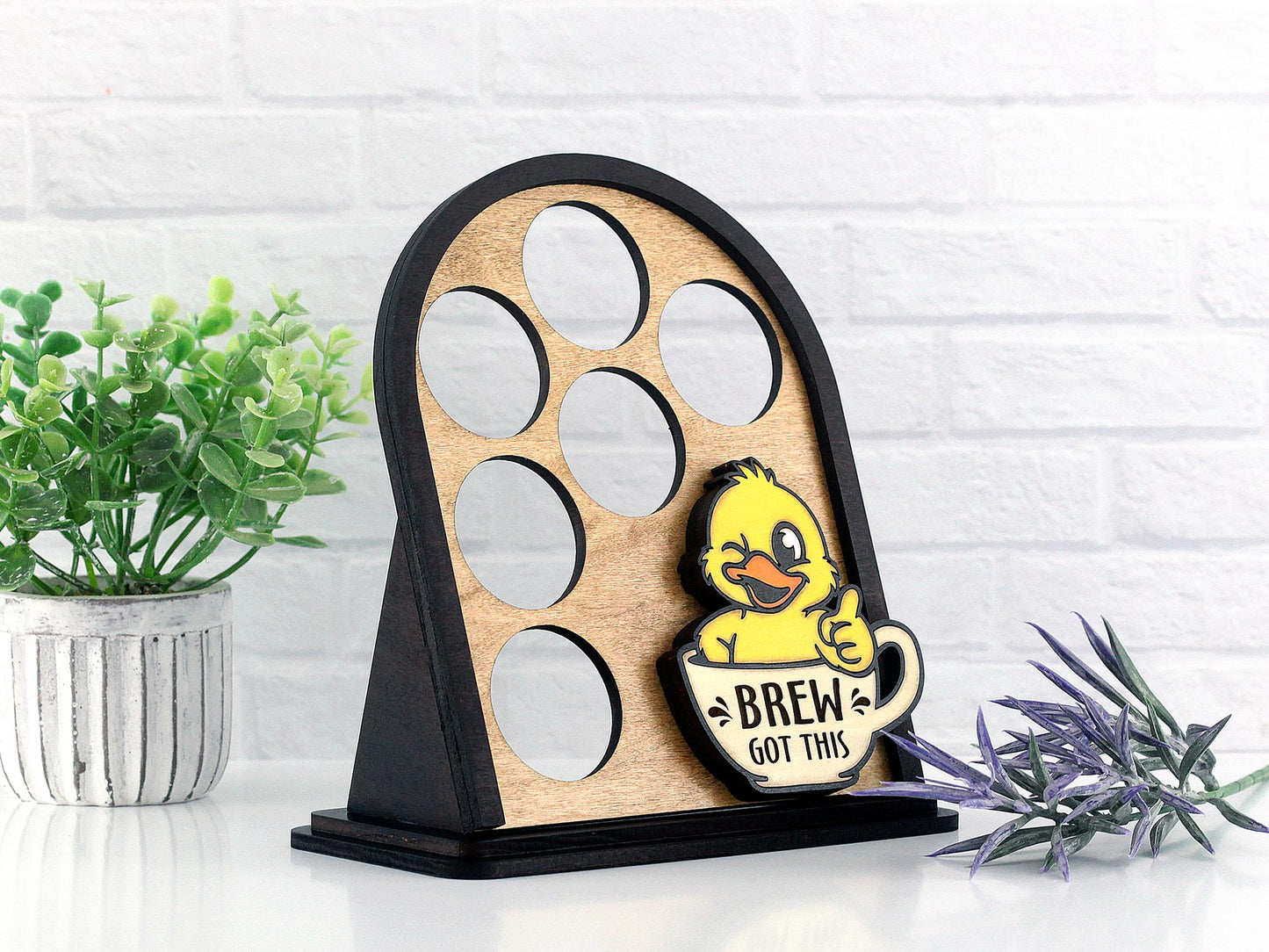 Wooden coffee pod display with a cute duck design on a white surface with plants.