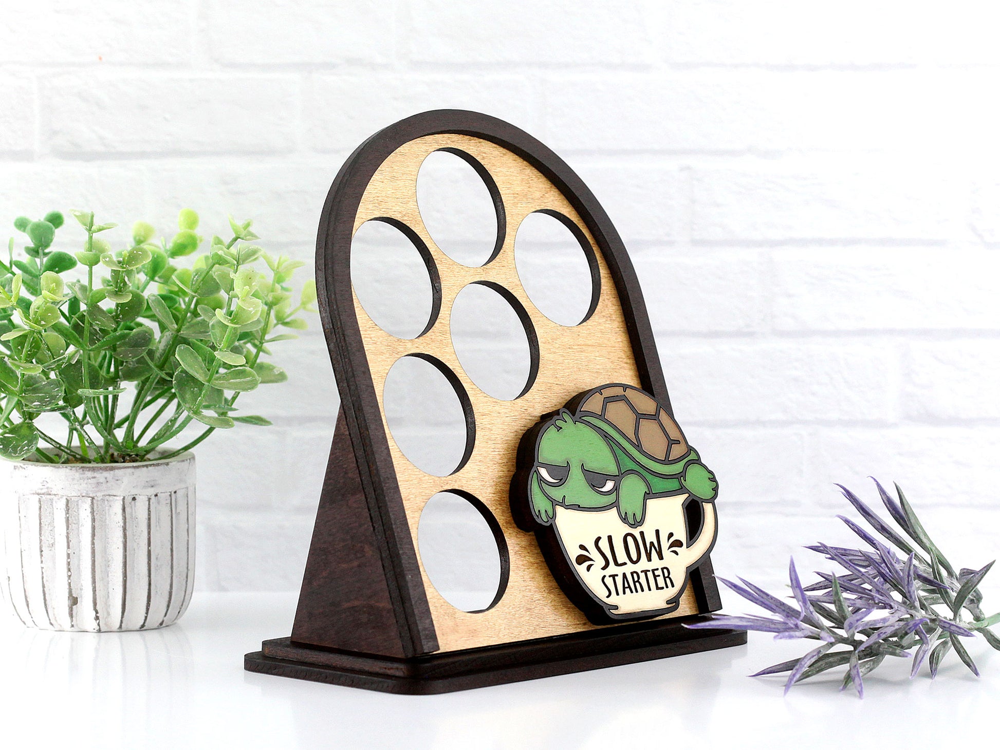 Wooden coffee pod display with turtle design and 'Slow Starter' text, placed on a white surface with plants.
