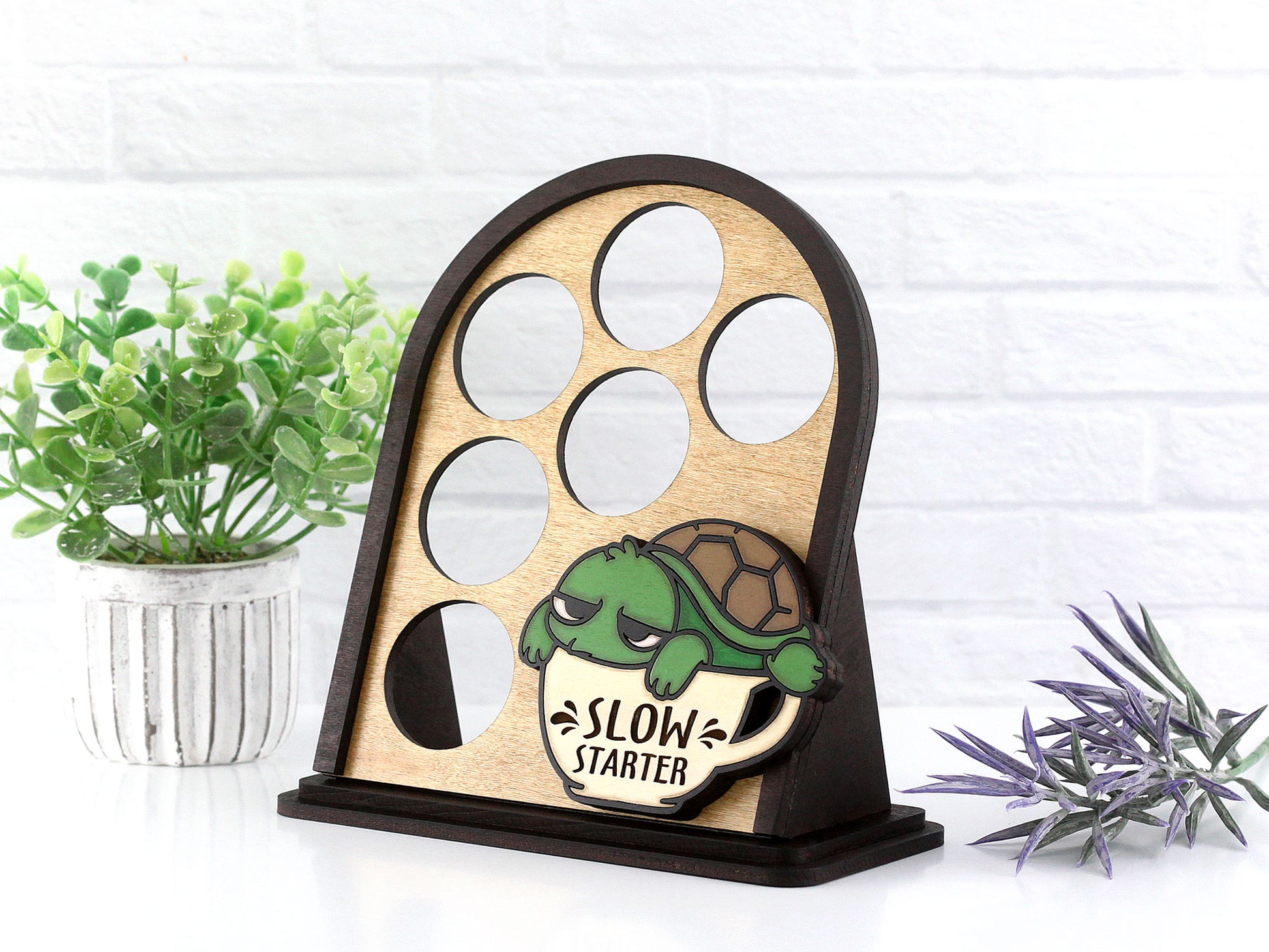 Wooden k cup organizer with turtle design and 'Slow Starter' text, placed on a white surface with plants.