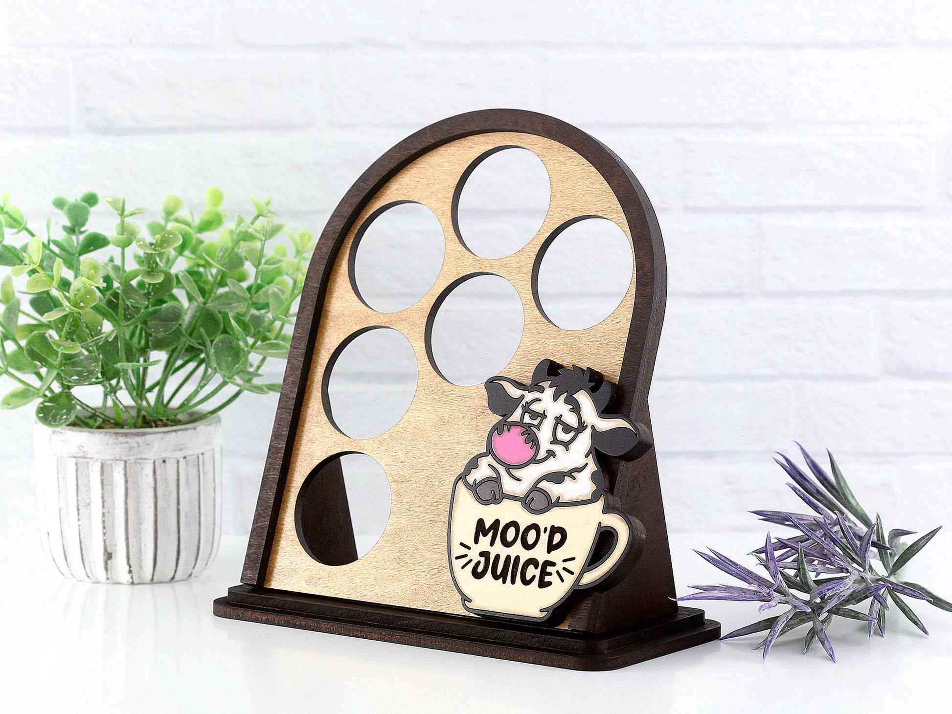 Wooden k cup holder with cow design and 'Mood Juice' text, placed on a white surface with plants.