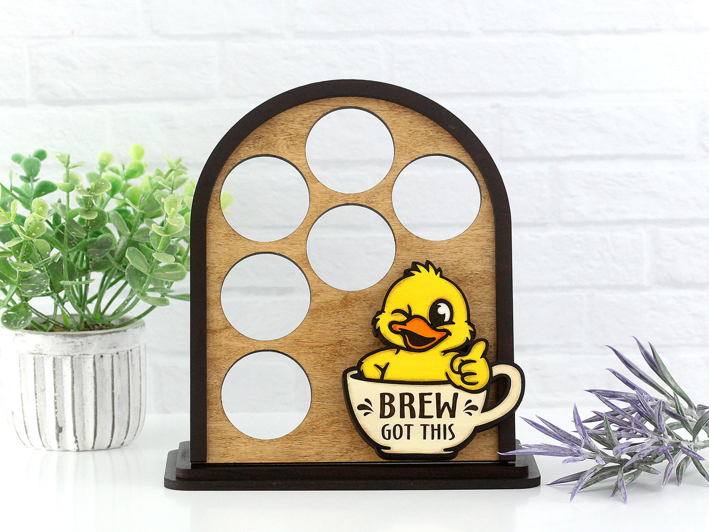 Wooden coffee pod holder with a duck design and 'Brew Got This' text, placed on a white surface with plants.