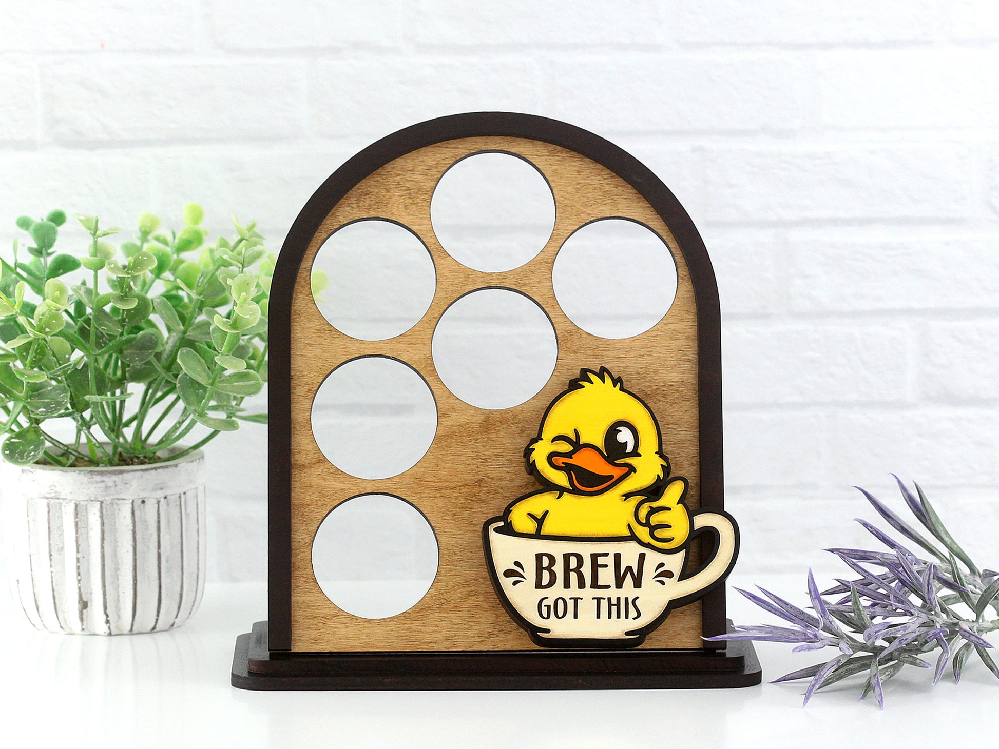 Wooden coffee pod holder with a duck design and 'Brew Got This' text, placed on a white surface with plants.