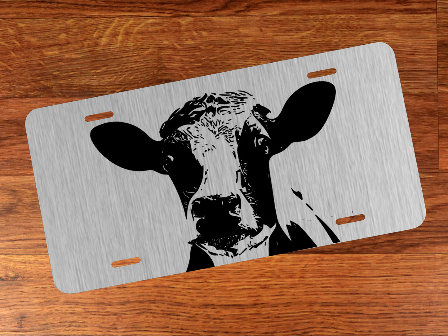 Metallic license plate with a cow design on a wooden surface