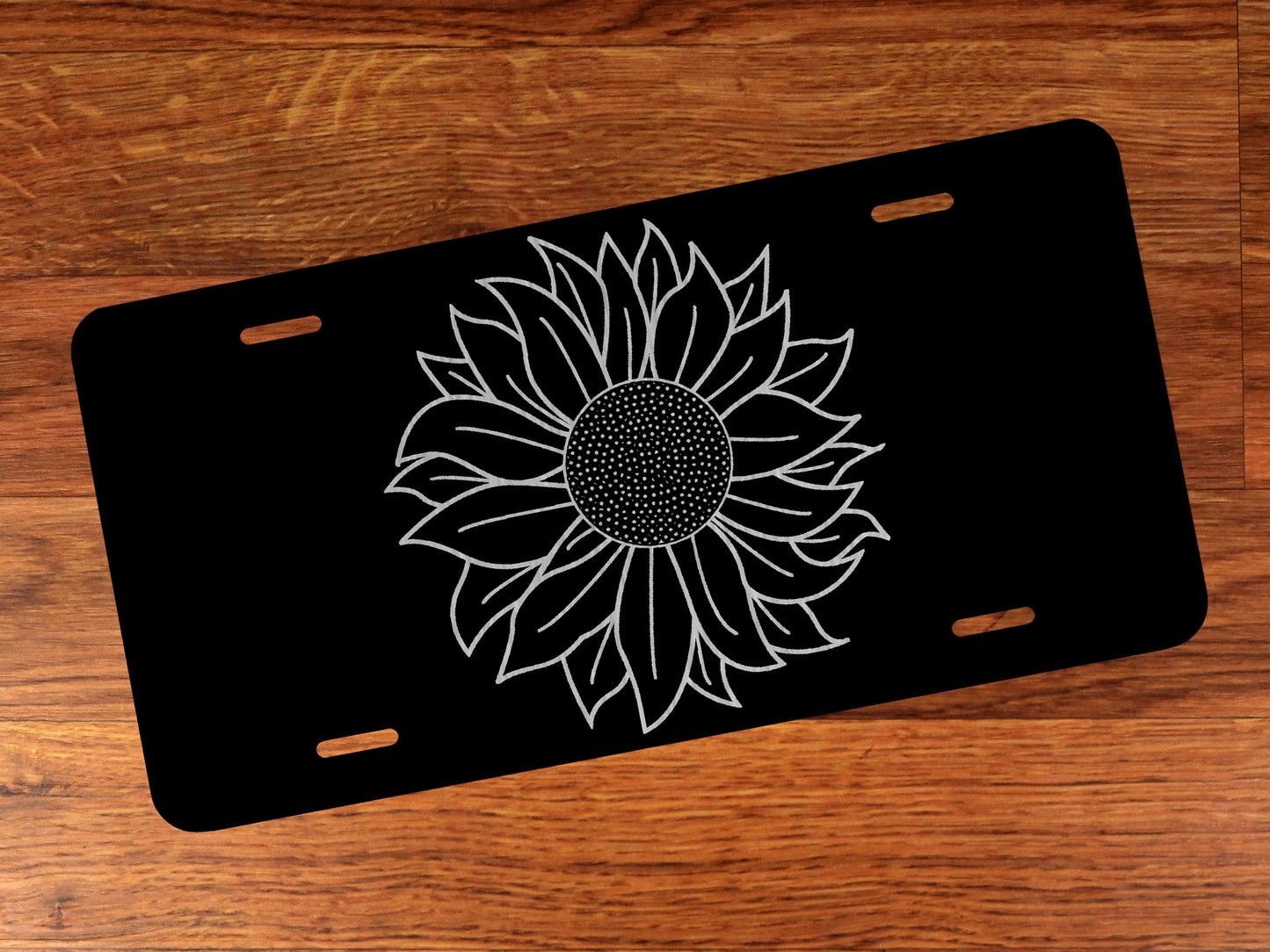Black license plate with a silver sunflower design on a wooden surface