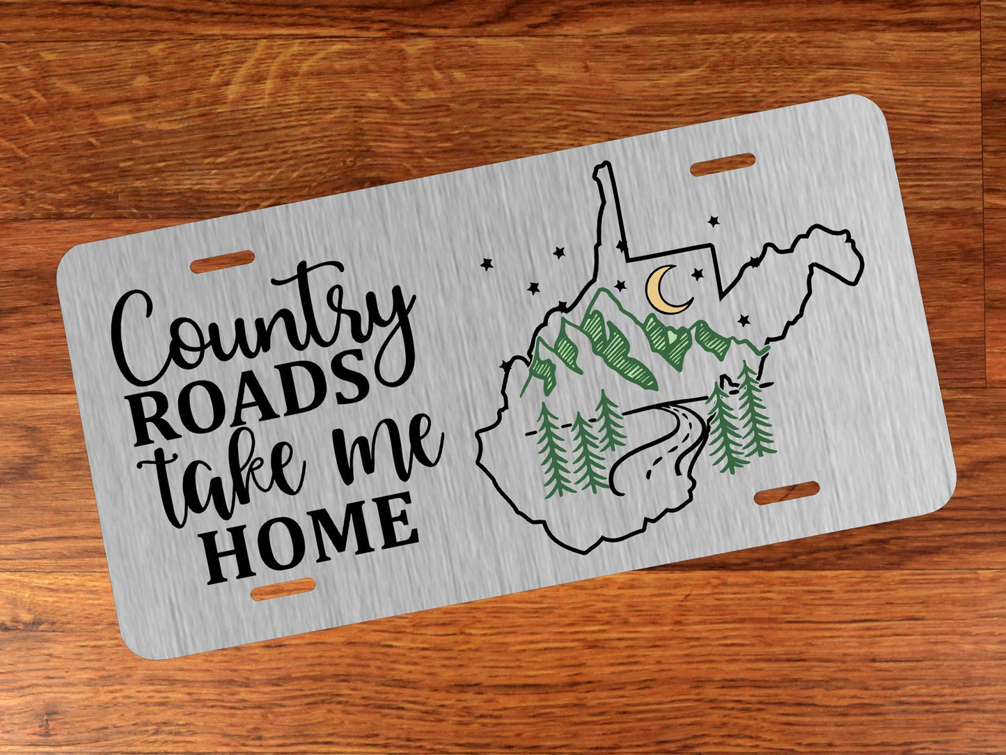 Silver license plate with 'Country Roads take me Home' text and West Virginia outline on a wooden surface