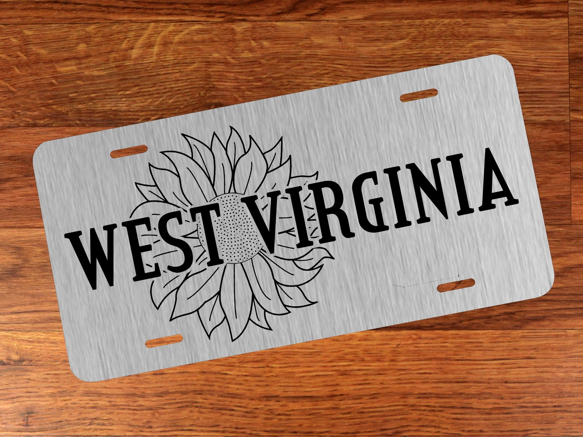 Silver license plate with 'West Virginia' and sunflower design on a wooden surface